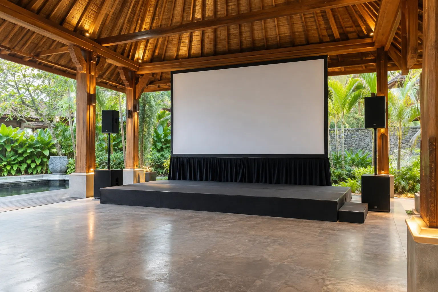 Low stage and blank presentation screen inside a covered tropical event pavilion