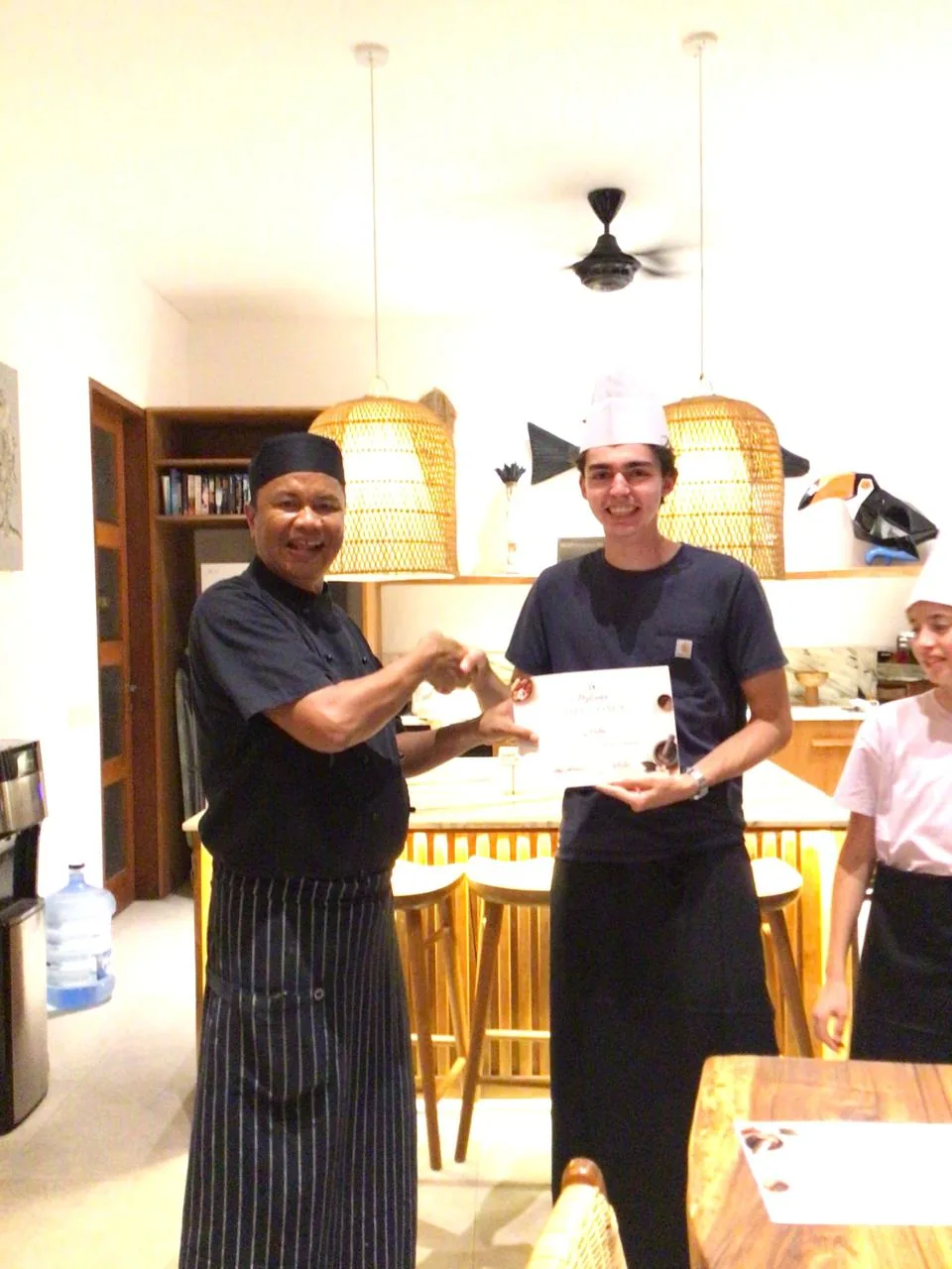 Chef shaking a guest’s hand while presenting a filled cooking-class diploma in a Bali villa