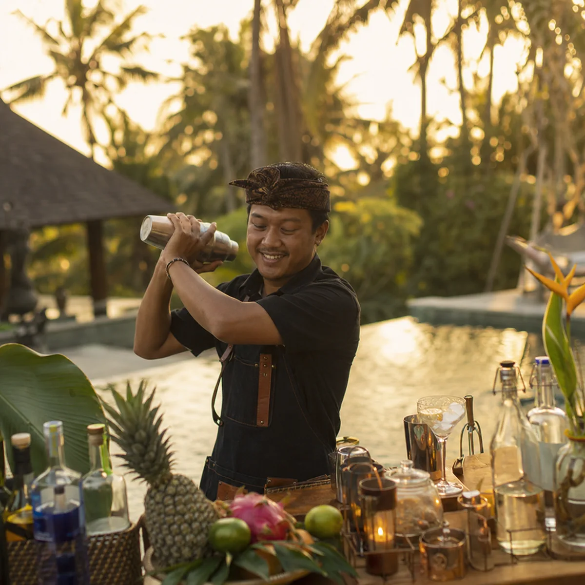 Balinese mixologist shaking a cocktail at a Bali villa bar at golden hour