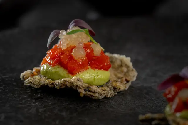 Canapé of avocado cream and diced tomato on a puffed crisp
