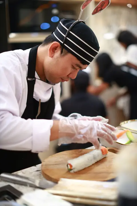 myCHEF chef in gloves rolling sushi on a wooden board